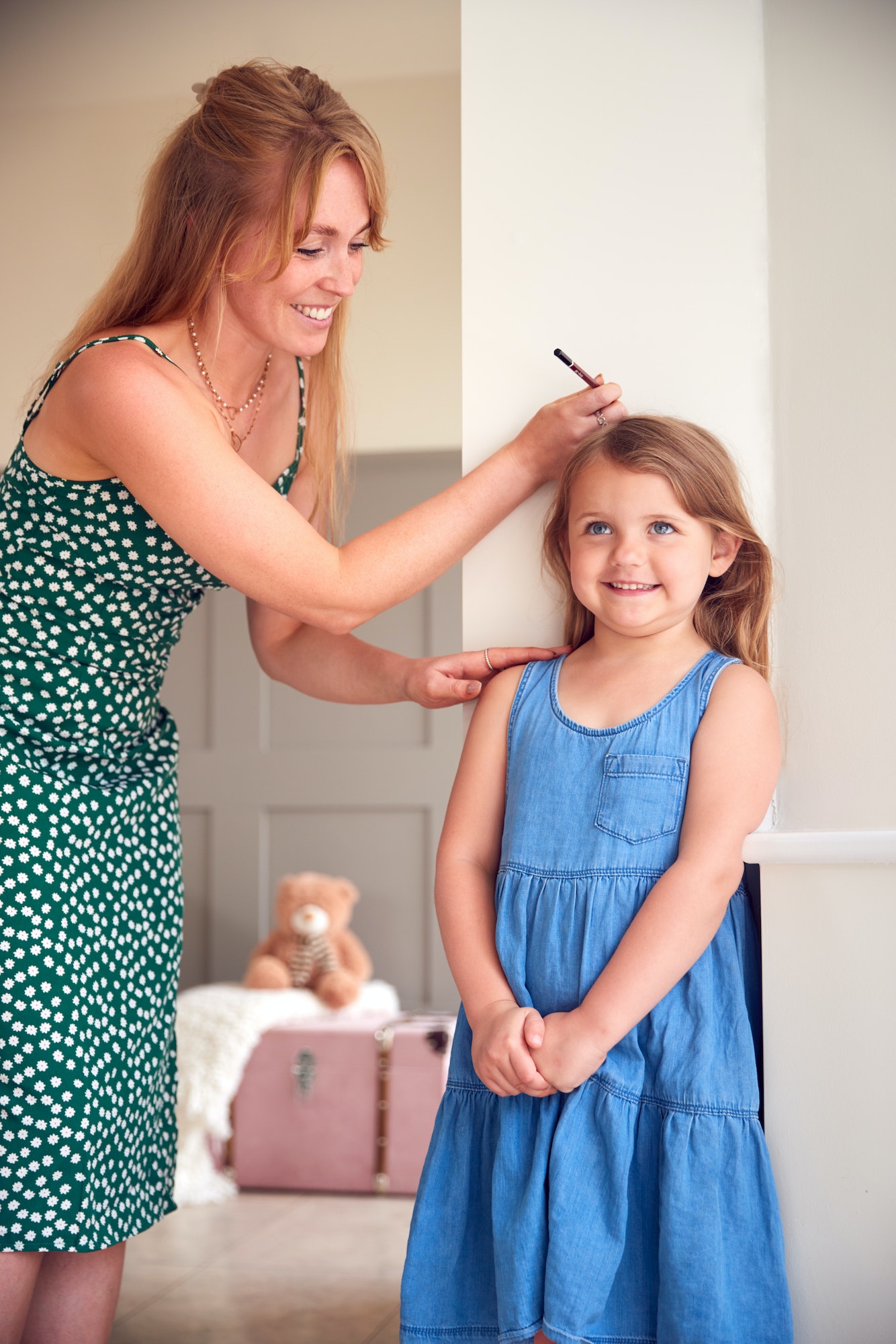 Mother Measuring Daughter's Height And Marking On Wall At Home